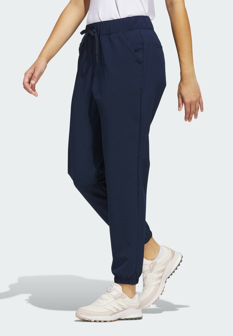 Marineblå joggerbukser med elastisk talje og snor, med sidelommer og elastiske manchetter. Båret med lysfarvede sneakers.