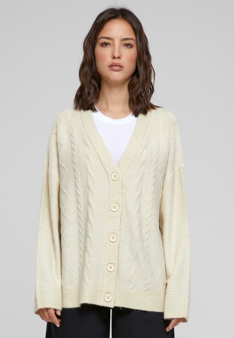 Cremfarbener Kabelstrickcardigan mit V-Ausschnitt, ausgestattet mit fünf großen beigen Knöpfen, abfallenden Schultern sowie gerippten Ärmelbündchen und Saum.