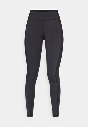 Black leggings made from stretchy material. High-rise waistband, smooth texture, featuring patterned accents at the lower leg.