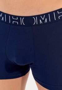 Mörkblå boxershorts i mjukt tyg med en bred elastisk midjeband som har vit text. Åtsittande design, mjuk struktur och sömfria sidor.