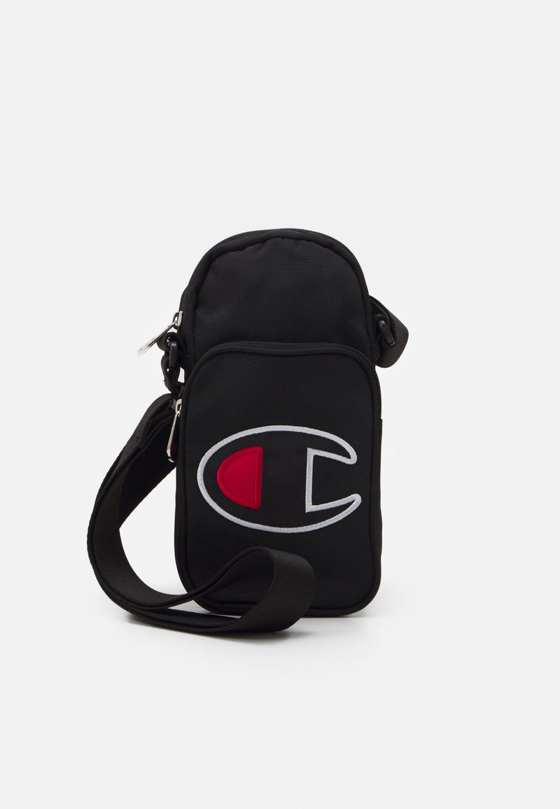 Sac bandoulière noir avec sangle réglable, poche zippée à l'avant et grand logo blanc et rouge sur le panneau avant.