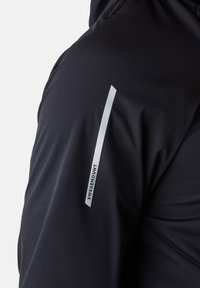 Schwarze technische Jacke mit glatter Textur, figurbetontem Schnitt und einem auffälligen weißen vertikalen Streifen mit dem Text "SWEDEMOUNT" auf dem Ärmel.