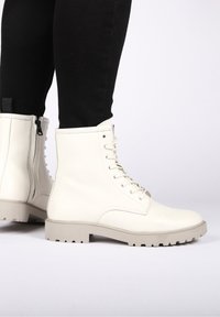 Bottines en cuir blanc avec une finition texturée, dotées de lacets, d'une fermeture éclair latérale et d'une semelle épaisse en caoutchouc gris avec un motif de crampons.