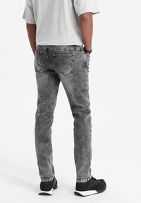 Miestne šedé deninové nohavice so zosvetleným vzhľadom, s piatimi vreckami a jemnými detailmi šitia, doplnené o čierne športové topánky.