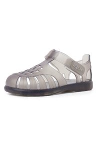 Sandal grigia traslucida con design aperto, caratterizzata da motivi intagliati, cintura regolabile e suola in gomma nera.