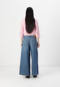 Blue wide-leg denim jeans with a high waist, featuring a brown leather patch, two back pockets, and a relaxed fit.