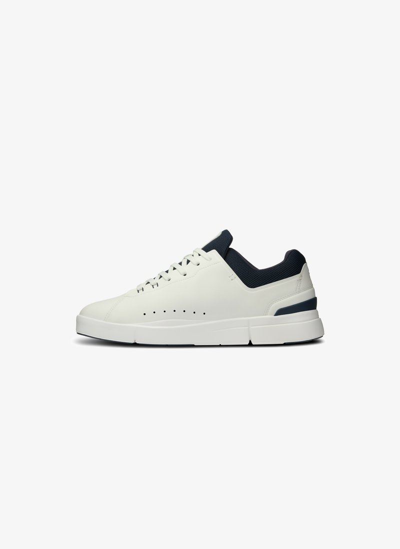 Zapatilla de cuero blanca con un collar de malla en azul marino, diseño curvado, detalles perforados en el costado y una suela gruesa blanca con acentos en azul marino.