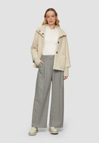 Creme gekleurde jas met een oversized kraag en knopen, gecombineerd met grijze wijde broek en beige platform schoenen. Wit topje eronder.