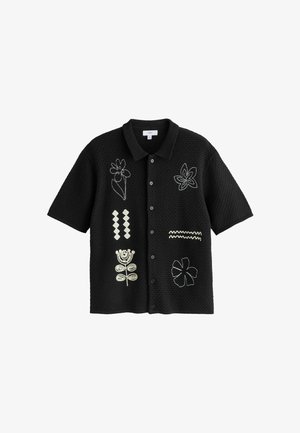 Musta lyhythihainen nappipaita, jossa on tekstuurinen neulos ja valkoinen abstrakti kukka- ja geometrinen kirjonta edessä.