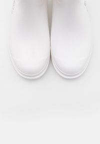 Paire de bottes de pluie en caoutchouc blanches et propres, à bouts arrondis lisses, photographiées de dessus sur un fond blanc.