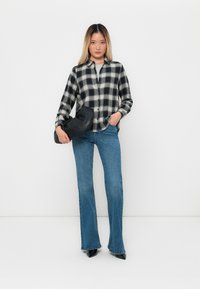 Svart og hvitt rutete skjorte med knappelukking, blå utsvingte jeans og svart veske holdt under armen. Glatt stoff og tettsittende design.