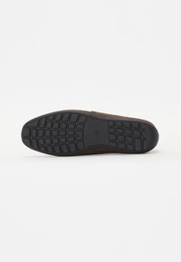Hnědá semišová slip-on obuv s texturovanou černou gumovou podrážkou s mřížkovým vzorem pro lepší trakci. Minimalistický design bez viditelného kování.