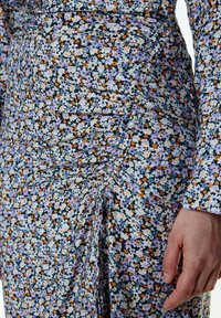 Bloemjurk met een zwarte achtergrond en kleine bloemen in paars, oranje en wit. Gerimpelde textuur aan de zijkant, lange mouwen.
