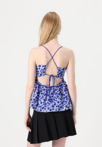 Blauwe bloempatronen top met spaghettibandjes, gathers aan de achterkant en striksluiting. Gepaarde met een zwarte geplooide rok.