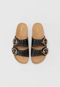 Sandales noires à glissière avec deux larges sangles, des clous dorés et de grandes boucles circulaires. La semelle est marron, avec une surface texturée.