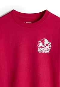 Camiseta de algodón roja con cuello redondo. Presenta un logo gráfico blanco con el texto "VANS OFF THE WALL" en el lado izquierdo del pecho. Textura suave.