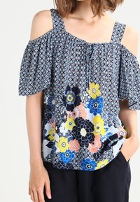 Bluzka w kwiatowy wzór z odkrytymi ramionami, w niebiesko-biała-żółtej kolorystyce, wykonana z luźnego, miękkiego materiału.