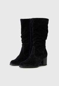 Bottines en daim noir avec un design décontracté, une fermeture éclair sur le côté et un talon carré structuré. Texture douce et bout arrondi.