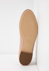 Chaussure en cuir rose clair avec une tige lisse, un bout arrondi et une semelle en caoutchouc marron comportant des rainures texturées. Logo visible sur la semelle.