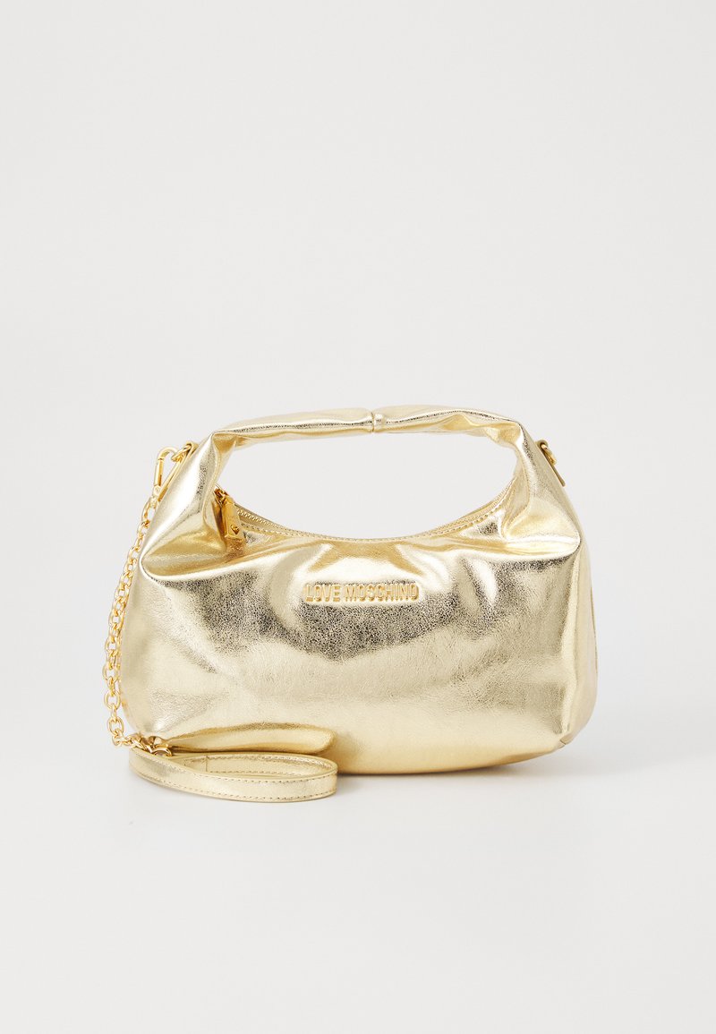 Gullfarget metallic håndveske med avrundet design, med en kort håndtak og avtakbar kjernesnor. Merkenavnet er preget på fronten.