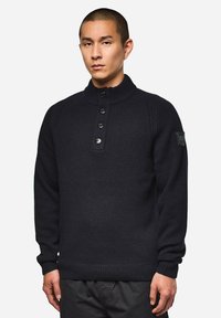 Dunkelblau gestrickter Pullover mit hohem Kragen, fünf Knöpfen und gerippten Bündchen. Mit Schulterdetails und einem Logo-Patch am Ärmelt.