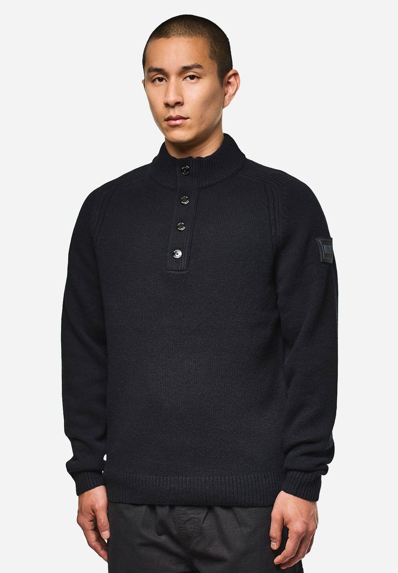 Dunkelblau gestrickter Pullover mit hohem Kragen, fünf Knöpfen und gerippten Bündchen. Mit Schulterdetails und einem Logo-Patch am Ärmelt.