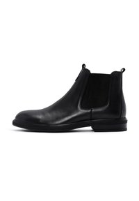Botín Chelsea de cuero negro con paneles laterales elásticos, puntera redondeada y una suela de goma texturizada y baja. Incluye tiradores para facilitar el calzado.