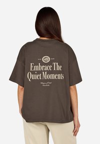 Czarna, bardzo duża bawełniana koszulka z krótkim rękawem z białym napisem na plecach „Przyjmij ciche chwile” oraz dodatkowymi nadrukowanymi detalami.