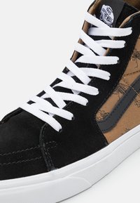 Baskets montantes en suède noir, textile marron avec motif floral, lacets blancs et bande latérale noire avec logo. Semelle en caoutchouc blanche.