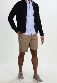 Marinblå zip-upp tröja, ljusblå skjorta med knappar, khakishorts, grå sneakers. Har en stilren design och en avslappnad, bekväm passform.