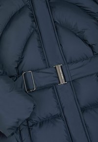 Marinblå puffjacka med kviltad design, justerbart bälte med metallspänne och en texturerad, isolerad tygfinish.