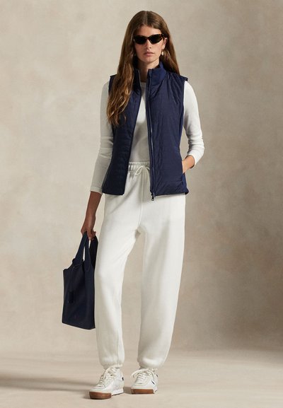 Μπλε σκούρο γιλέκο με ραφές, λευκό μακρυμάνικο μπλουζάκι, λευκή φόρμα και λευκά αθλητικά παπούτσια με ταμπά σόλες. Το αξεσουάρ περιλαμβάνει μια μπλε σκούρα τσάντα tote.