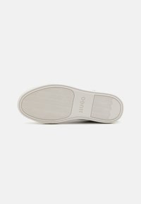Semelle de chaussure en caoutchouc blanche avec motif ondulé texturé, logo "HUGO" en relief et un design de bord lisse.