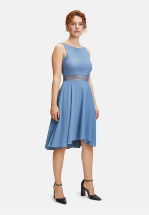 Blaues ärmelloses Kleid mit strukturiertem Oberteil und Spitzenverzierung an der Taille, mit einem fließenden Rock und knielangem Saum. Schwarze High-Heels.