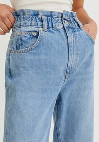 Jeans de mezclilla azul claro con una cinturilla fruncida, que presentan bolsillos frontales y mínimos detalles de costura. La tela tiene una textura suave.