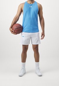 Maglietta atletica blu senza maniche, pantaloni corti bianchi con logo, tiene un pallone da basket Spalding. Scarpe da ginnastica bianche e calze corte completano l'outfit.