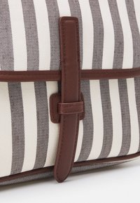 Bolsa de tela a rayas en tonos beige y marrón con una correa y acentos en cuero marrón. Presenta un diseño elegante con rayas horizontales y detalles cosidos.