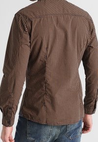 Camisa a cuadros marrón y beige con mangas largas, puños con botones, dobladillo curvado y diseño con canesú en la espalda. La tela parece ligera.
