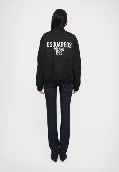 Veste bomber en quilt noir avec l'inscription blanche "DSQUARED2 MILANO 1995" dans le dos. Manches et ourlet côtelés. Portée avec un jean foncé.