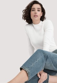 Weißes langärmeliges, geripptes Oberteil mit hohem Kragen, kombiniert mit lässigen, hellblauen Denim-Jeans im entspannten, verkürzten Schnitt.