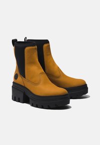 Gelbe Lederknöchelstiefel mit einem schwarzen elastischen Seitenpaneel und einer dicken schwarzen Außensohle mit einem robusten Profil.