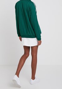 Grön randig jacka med ribbat krage och ärmslut, ihop med en vit kjol och vita sneakers. Fokusera på det strukturerade tyget.