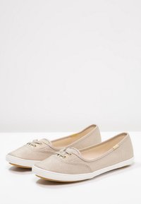 Ballerines en toile beige avec une surface texturée, un bout rond et des semelles en caoutchouc blanches. Équipées d'œillets dorés et d'un design de lacets minimaliste.