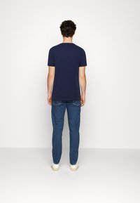 Tricou bleumarin cu mânecă scurtă, din material de bumbac, cu o croială clasică. Asortat cu blugi blue denim și adidași albi.