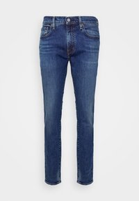 Jean en denim bleu pour homme, coupe slim, style cinq poches, taille boutonnée et détails délavés le long des cuisses et des genoux.