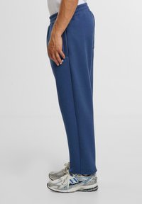 Navyblauwe trainingsbroek gemaakt van een katoenmix, met zijzakken en een elastische tailleband, gecombineerd met zilveren en blauwe hardloopschoenen.