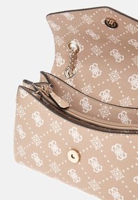 Lille beige håndtaske med hvid mønstret logo-print, guld kædestropp, og indvendig lynlås-lomme, vist åben fra oven.