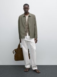 Oliven grøn letvægtsjakke, beige cardigan, hvide bukser, brun ruskindstaske og sorte flip-flops. Enkle, rene linjer og neutrale farver.
