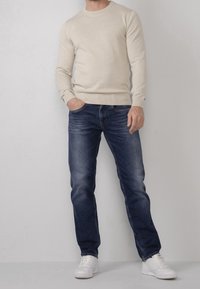 Maglione a maglia beige chiaro con maniche lunghe, abbinato a jeans in denim blu scuro e sneakers bianche; design comodo e texture visibile.