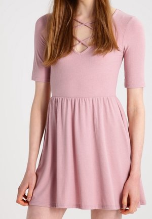 Robe rose côtelée avec un corsage ajusté, des manches courtes et une jupe évasée. Présente un décolleté en V avec des bretelles croisées au niveau de l'encolure.